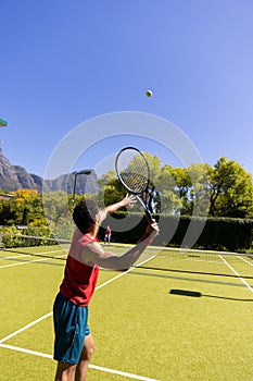 Biracial man with tennis racket returning ball to player on sunny outdoor tennis court, copy space