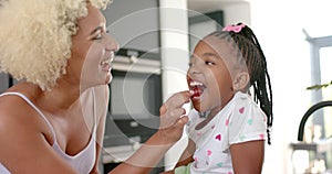 Biracial mom and daughter share joyful moment with strawberry at home.