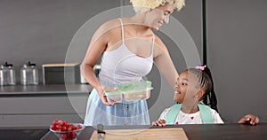 Biracial mom and daughter share a moment in kitchen with fruit.
