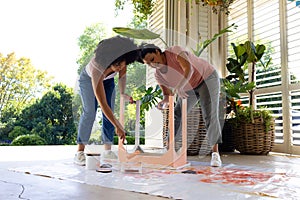 Biracial mother and adult daughter are painting a chair pink outside at home as an upcycling project