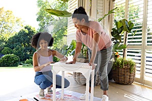 Biracial mother and adult daughter are painting furniture outside at home as an upcycling project