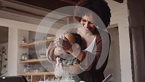 Biracial mother and young daughter clapping with flour on their hands while baking in modern-styled kitchen