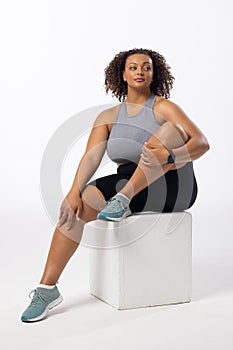 Biracial plus size model with curly hair holds leg on white background, copy space