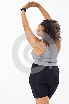 Biracial plus size model stretches arms up, in sports gear on white background