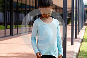 Biracial schoolgirl smiling, looking down at her top in sunny schoolyard copy space