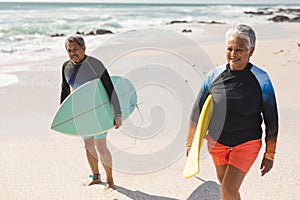 Biracial senior couple with surfboards walking at beach during sunny day