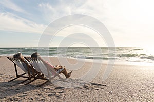 Biracial senior man and woman relaxing while sitting on folding chairs at beach