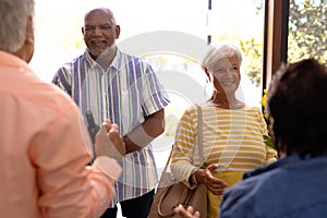 Biracial seniors welcoming cheerful friends standing at doorway in nursing home, copy space