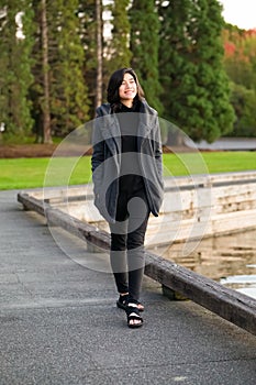 Biracial teen girl in gray jacket  walking along water park
