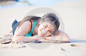 Biracial teen girl lying on sandy beach, resting and smiling