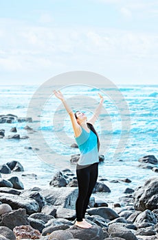 Biracial teen girl on rocks by ocean praising God