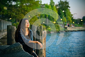 Biracial teen girl  sitting  looking out over lake at sunset