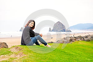 Biracial teen girl sitting near ocean in Pacific Northwest