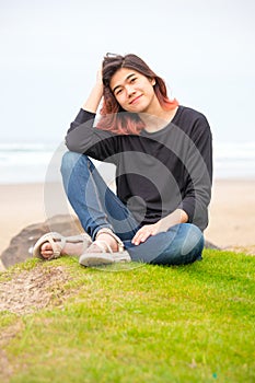 Biracial teen girl sitting near ocean in Pacific Northwest