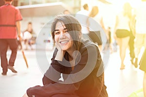 Biracial teen girl sitting by sidewalk, people walking in background