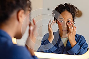 Biracial woman in bathrobe wearing eye mask in bathroom