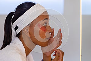 Biracial woman in bathrobe wearing eye mask in bathroom