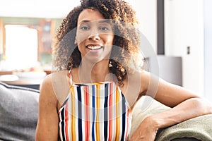 Biracial woman with curly brown hair smiles warmly, wearing a colorful striped top