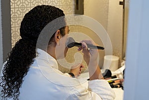 Biracial woman sitting in a hotel room bathroom putting on makeup