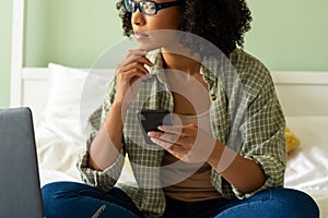 Biracial woman using laptop and smartphone on bed in bedroom