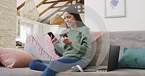 Biracial woman using smartphone and holding credit card in living room