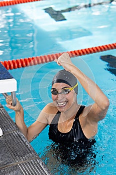 Biracial young female swimmer with a bright smile is holding onto the pool edge indoors photo
