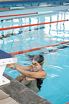 Biracial young female swimmer holding onto swimming pool edge, resting indoors, copy space