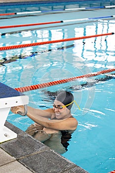 Biracial young female swimmer holding onto swimming pool edge, resting indoors, copy space photo