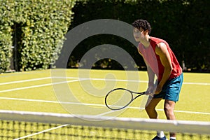 Biracial young man holding tennis racket and standing on grassy field at tennis court