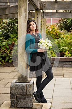 Biracial young teen bridesmaid holding flower bouquet outdoors under pergola