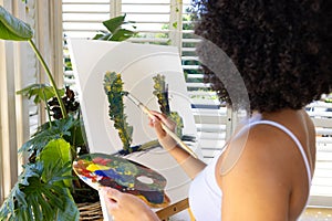 Biracial young woman painting on canvas at home, focusing intently photo