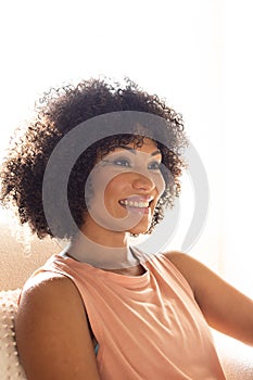 Biracial young woman sitting at home, looking away, smiling gently photo