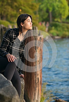 Biracial young woman sitting  looking out over lake at sunset