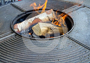 Birch firewood burns in the center of a round metal barbecue table