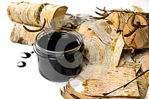 Birch tar or pitch in a jar and birch tree bark on white background. Wood tar