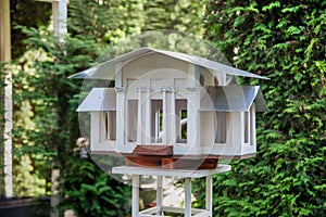 Bird feeder in the form of a wooden house with a roof and columns of white color on a background of greenery