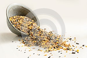 Bird food from mixed seeds like sunflower, corn, millet and more, are falling out of a bowl on a light background, copy space