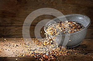 Bird food for winter feeding, mixed seeds like sunflower, corn, millet and more are falling out of a bowl on a rustic wooden board