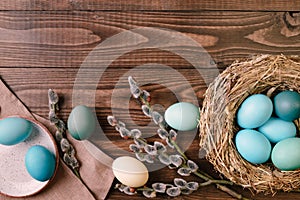 Bird nest with turquoise easter eggs and willow branch on wooden desk