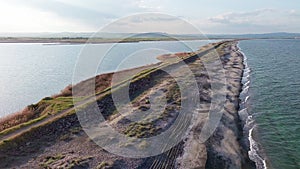 Bird's eye view of beach with sand, grass and stones washed by bay of Black Sea and lake under sky in sunset light