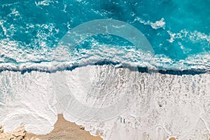 Bird's-eye view of a couple of people on a sandy beach with turquoise clear water with foaming big waves. Drone shot