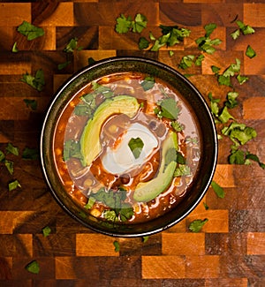 Bird's eye view of an orange creamy chicken enchilada soup with avocado sour cream and cilantro on a cutting board