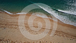 bird\'s-eye view of seashore, blue waters break with white foam in waves on an empty sandy beach
