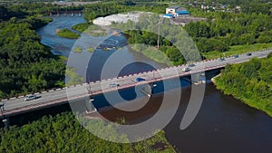 A bird's-eye view of summer. Clip. The bridge on which cars drive over the river, next to which there is a forest behind