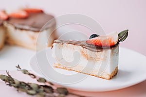 Bird's milk cake with chocolate decorated with strawberries and grapes with piece on white plate on pink background