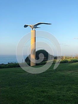 A bird statue perched on a high pole against natural landscape backdrop