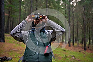 Bird watcher on the hunt. Handsome man using his binoculars to scan the surrounding forest for bird life.