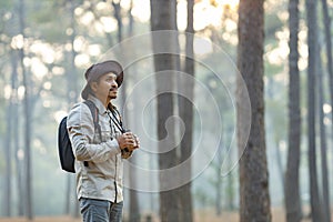 Bird watcher is looking through binoculars while exploring in the pine forest for surveying and discovering the rare biological