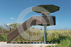 Bird watcher tower in Ebro Delta wetland area with rice field against a cloudy blue sky. Empty copy space