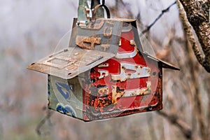 Birdhouse made with various old license plates hanging from a tree